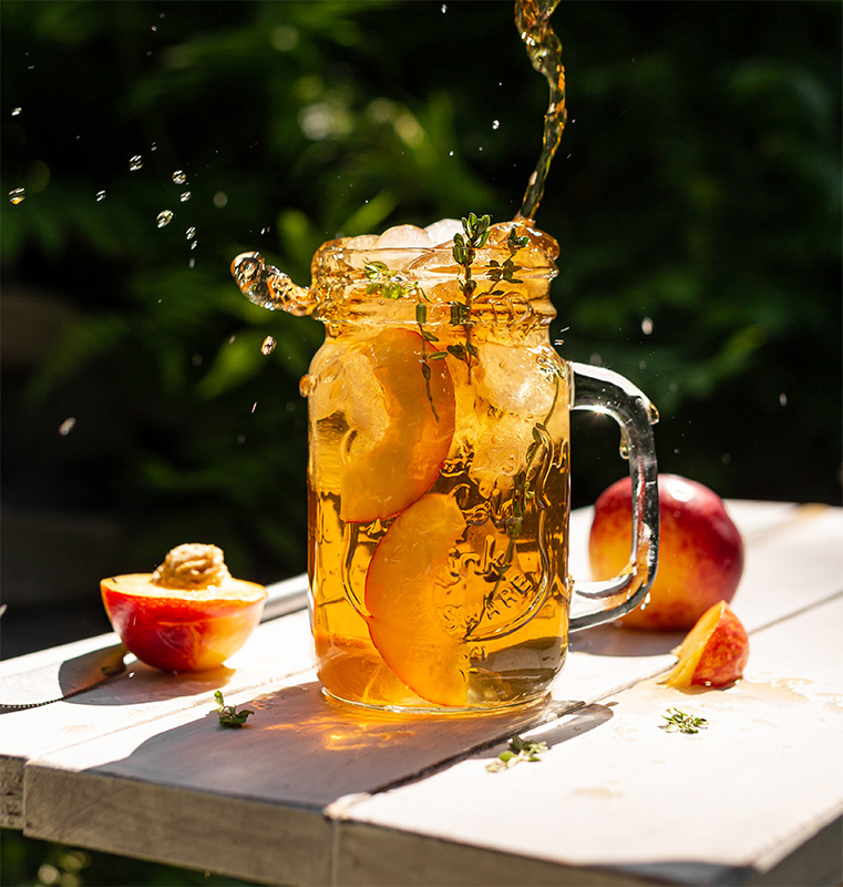 a glass of tea being poured with slices of fresh peach a glass of tea being poured with slices of fresh peach